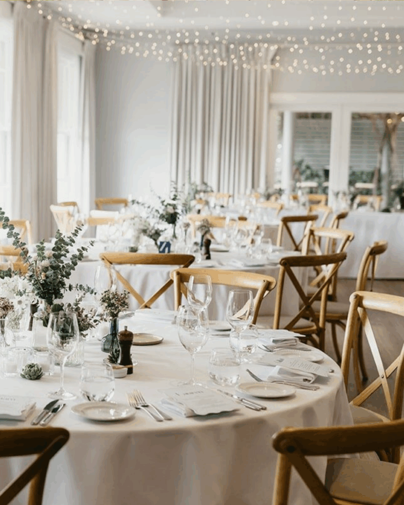 100 Breathtaking and Exclusive Australian Wedding Venues on every Couples Wish List! 1 Elegant dining setup at The Bells at Killcare, featuring wooden chairs, white tablecloths, and floral centerpieces, with twinkling fairy lights enhancing the romantic atmosphere for weddings.