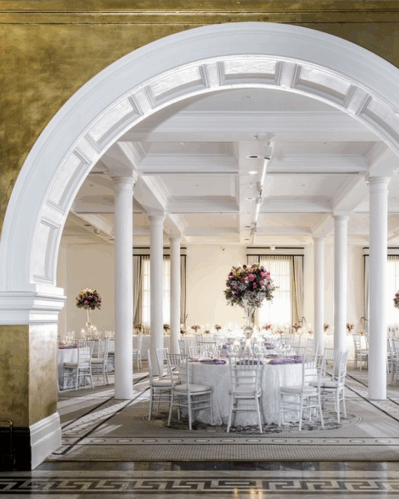 100 Breathtaking and Exclusive Australian Wedding Venues on every Couples Wish List! 34 Elegant wedding reception setup at InterContinental Sydney featuring round tables adorned with floral centerpieces, white chiavari chairs, and sophisticated decor in a heritage venue with gold accents.
