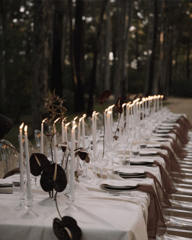 100 Breathtaking and Exclusive Australian Wedding Venues on every Couples Wish List! 7 Elegant outdoor dining setup with white candles, decorative plants, and glassware, set amidst a serene forest backdrop, ideal for romantic weddings at Jackson Ranch.