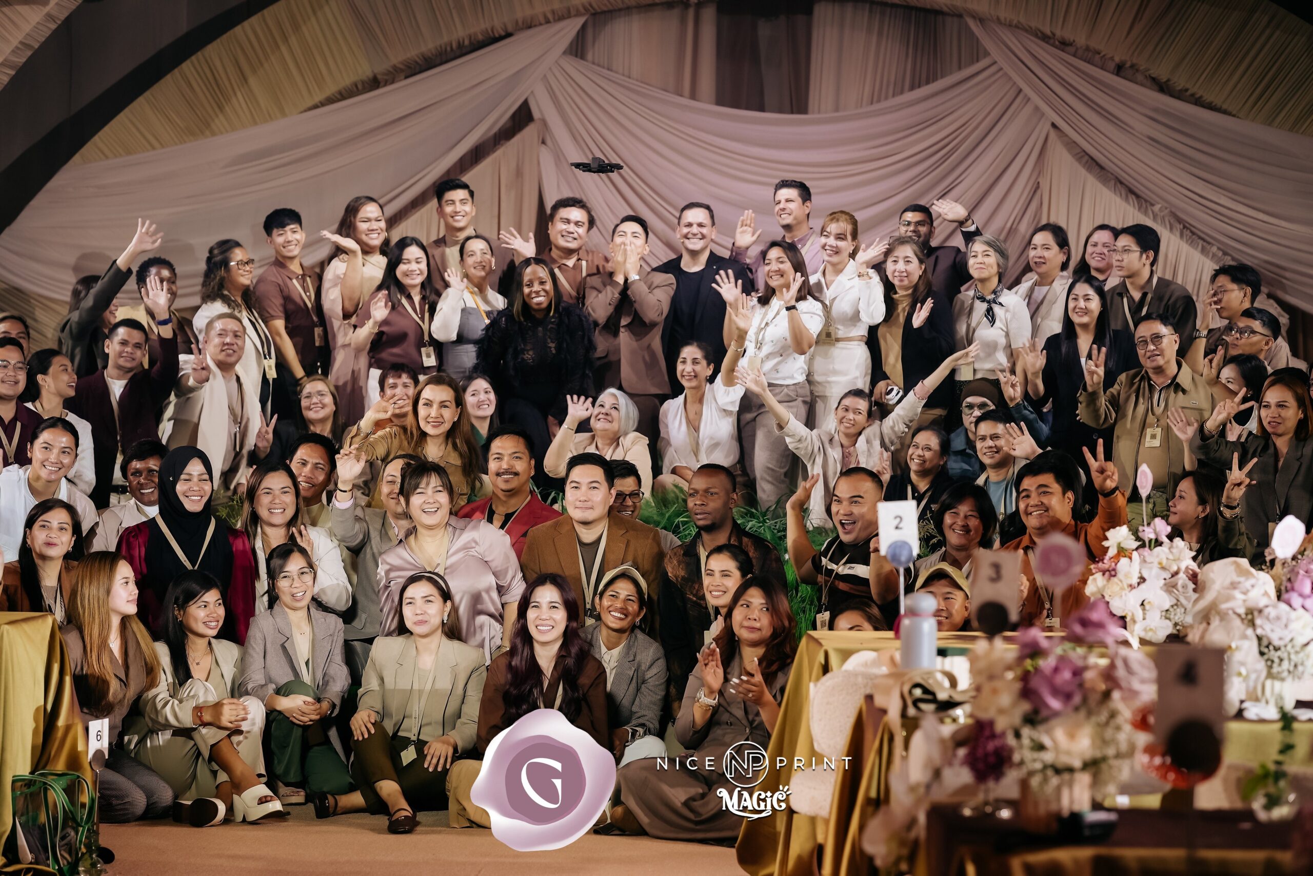 Group photo of wedding industry professionals celebrating at Gideon Hermosa’s Gala Night Extravaganza, featuring diverse attendees smiling and waving, with floral decorations and event branding visible.
