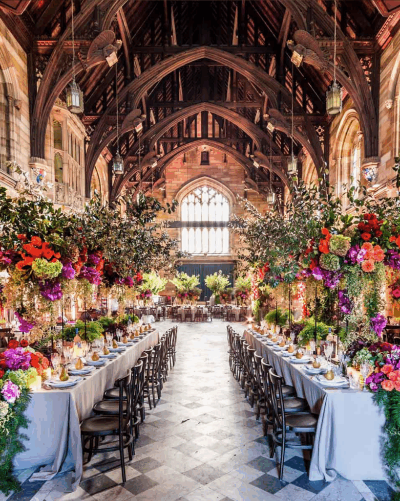 100 Breathtaking and Exclusive Australian Wedding Venues on every Couples Wish List! 5 Luxurious wedding reception setup in the Great Hall of Hostco Sydney, featuring long elegantly dressed tables adorned with vibrant floral arrangements, intricate table settings, and a grand architectural backdrop.