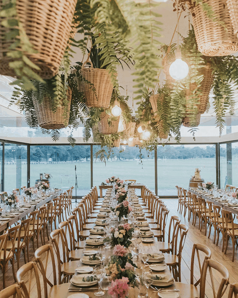 100 Breathtaking and Exclusive Australian Wedding Venues on every Couples Wish List! 50 Elegant dining setup in the Wisteria room at The Centennial Homestead, featuring long wooden tables adorned with floral centerpieces, surrounded by hanging plants and warm lighting, with panoramic views of the garden.
