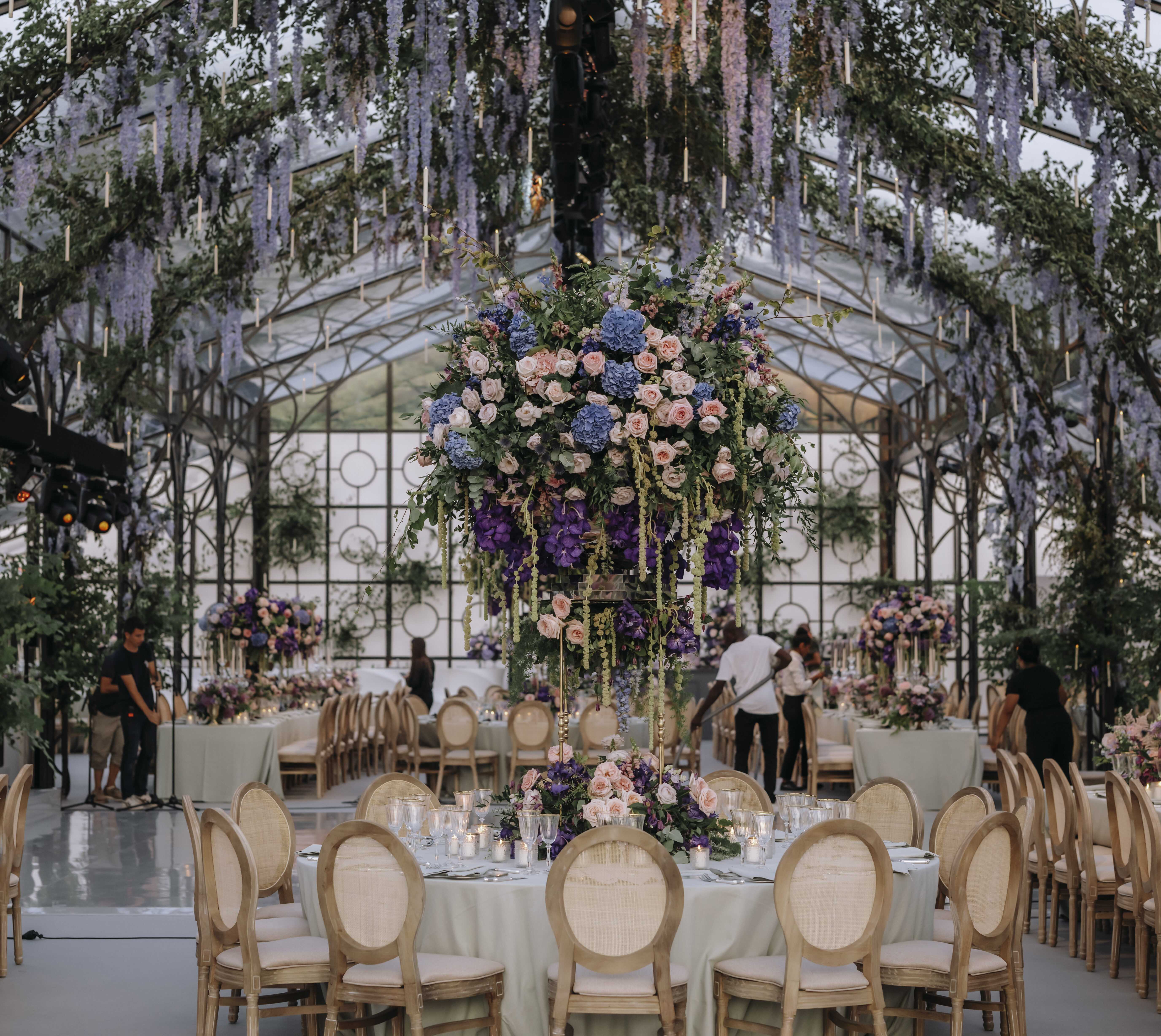 Elegant wedding reception setup with round tables adorned with floral arrangements, featuring hanging greenery and vibrant centerpieces in a beautifully decorated venue.